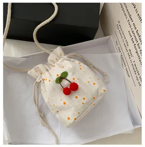 Gros plan détaillé sur le joli sac seau en toile brodé de marguerites avec pendentif cerise.