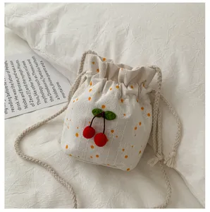 Vue rapprochée du sac seau à motif floral blanc avec cerises rouges et bandoulière tressée.