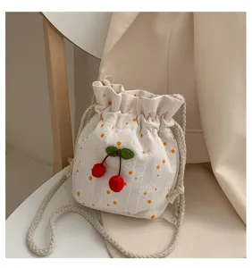 Vue détaillée d'un sac seau en toile blanche avec imprimé marguerites et charm de cerise rouge.