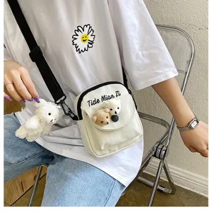 Detail shot of a cute canvas crossbody bag featuring lovely plush bear pendants and print.
