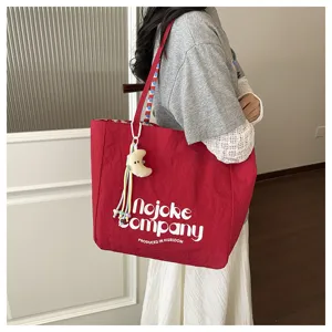 Vista dettagliata della borsa tote in tela rossa con stampa lettere e grazioso ciondolo luna.