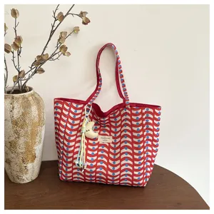 Dettaglio in primo piano della borsa tote in tela casual con stampa a onde rosse e ciondolo luna.