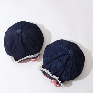Close-up of kids dark blue denim beret with delicate white lace trim and cute red plaid bow.