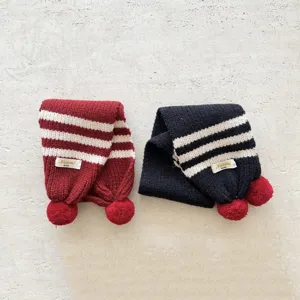 Primo piano dettagliato di sciarpa a righe lavorata a maglia per bambini con pon-pon rossi.