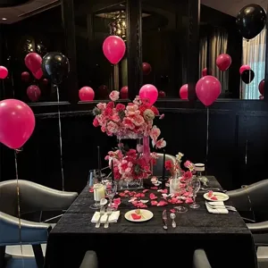 Detail view of pink and black party balloons table setting with flowers and rose petals.