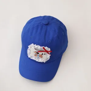 Detailed view of kids blue baseball cap with cute lace trim, cartoon dog patch, red bow.