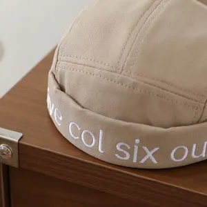 Detailansicht der beige Kinder Dockermütze mit sauberer weißer Stickerei auf dem Stoff.
