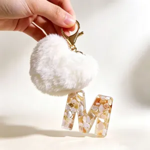 Nahaufnahme des Harzschlüsselanhängers mit Buchstabe M und flauschigem weißen Herzpompon.