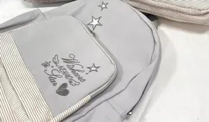 Dettaglio di uno zaino scolastico grigio in stile coreano con ricamo di stelle e tasca.