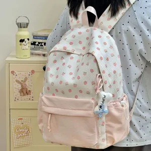 Dettaglio zaino rosa con stampa fragole, grazioso ciondolo cucciolo e stile studentesco.