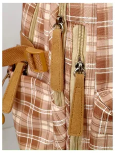 Detailed close-up view of vintage plaid backpack showing metal zippers and brown leather pulls.