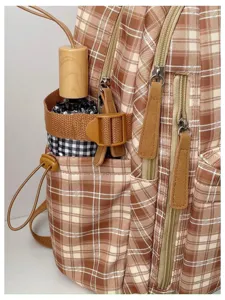 Detail view of the brown retro plaid backpack showing side pocket and zipper detail.