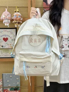 Vista detallada de una mochila escolar de lona con lindo parche de oso y detalles florales bordados.