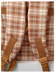 Close-up detail of the brown plaid backpack showing adjustable padded straps and sturdy buckles.