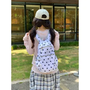 Detailed view of a cute Korean style white backpack with black polka dots, worn outdoors.