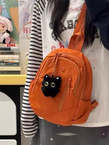 Close-up detail of a vibrant orange mini backpack featuring a plush black cat charm and nylon finish.