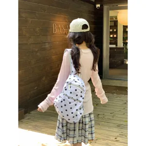 Close-up detail of cute white canvas school bag featuring classic black polka dot pattern.