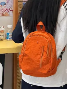 Close-up of vibrant orange casual backpack worn by person, showing zipper and fabric texture.