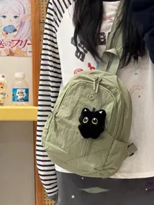 Small green nylon backpack and crossbody chest bag detail view, featuring cute black cat plush.
