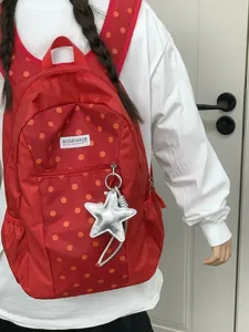 Vista detallada de una mochila roja de lunares con colgante de estrella plateada.