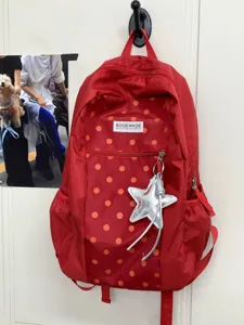 Vista detallada de mochila de lona roja con lunares, bolsillo frontal y colgante de estrella.