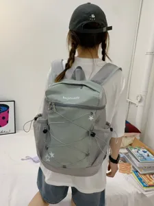 Detail view of the casual grey-green backpack featuring drawstring cords and side mesh pockets.