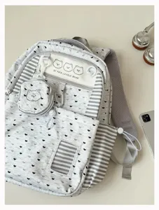 Detailed view of grey school backpack featuring cute heart patterns, stripes and bear patch.