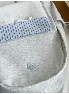 Primo piano dettagliato dello zaino grigio melange con tasca a righe ed elegante logo ricamato.