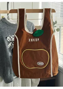 Detalle de la bonita mochila marrón en forma de manzana con hoja verde y bordado.