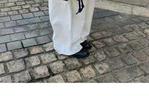 Detailed view of casual white trousers paired with black shoes on a scenic cobblestone street.