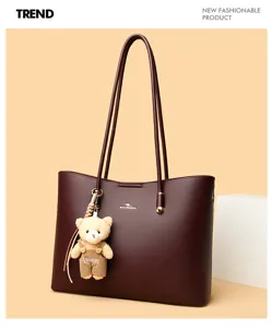 Detail van de bordeauxlederen shopper met smalle dubbele handgrepen en schattige berenhanger.