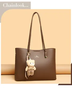 Detailopname van een bruine lederen totebag met lange handvatten en een schattige berenhanger.