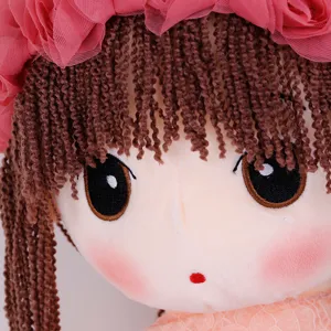 Simpatico giocattolo di bambola di peluche con capelli in filato marrone e copricapo floreale rosa.