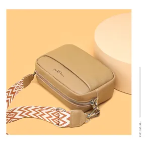 Genuine leather crossbody bag detail, chic square purse with wide patterned strap and zipper.