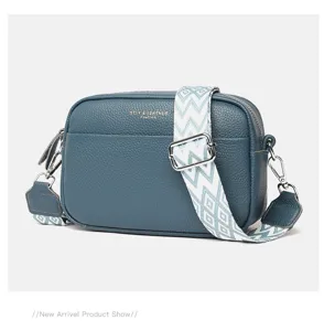 Detailed view of blue cowhide crossbody bag with stylish patterned wide strap and metallic hardware.