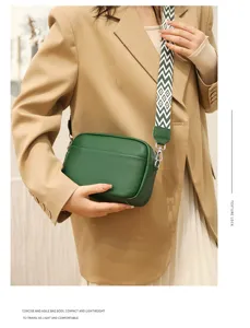 Detail shot of a green genuine leather crossbody bag with a wide geometric strap and metal hardware.