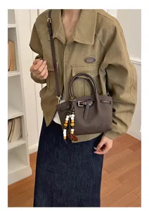 Élégant sac à main marron effet croco avec poignées supérieures et charm perlé chic.