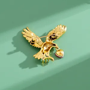 Detaillierte Nahaufnahme der goldenen Adler Brosche mit sicherem Pin und rotem Herzanhänger.