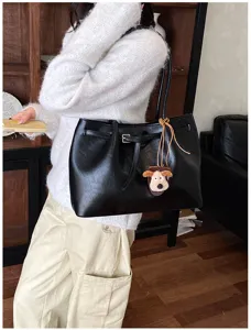 Detail view of the black leather tote bag featuring a cute dog charm and shoulder strap.