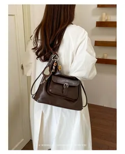 Detailansicht einer braunen Vintage-Umhängetasche mit Vordertasche und stilvollem Anhänger.