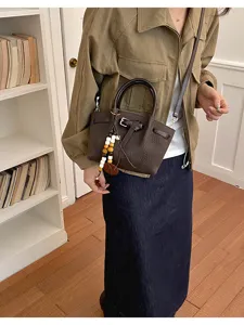 Sac à main marron texturé en cuir, sac bandoulière tendance avec poignée et détail de ceinture.