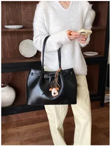 Detailed shot of stylish black PU leather tote bag with cute dog pendant and shoulder strap.