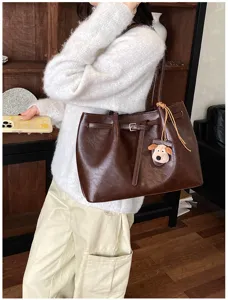 Detail shot of a brown leather shoulder tote bag, casual commuter style with cute puppy pendant.