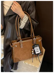 Detailed view of brown retro tote bag with leather and suede contrast panels and charm.