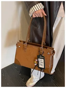 Detail view of a retro brown PU leather handbag featuring dual handles and a chic tag charm.