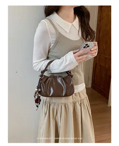 Vue détaillée du sac porté épaule plissé marron foncé brillant avec pendentif et texture.