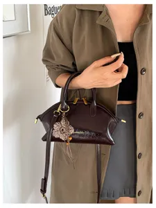 Sac à main en cuir vernis marron foncé avec pendentif fleur en tricot et bandoulière.