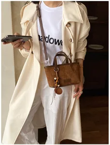 Detail shot of retro brown suede crossbody bag paired with trench coat for stylish look.
