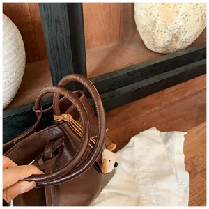 Brown leather tote bag detail showing handles, drawstrings and cute puppy plush charm.