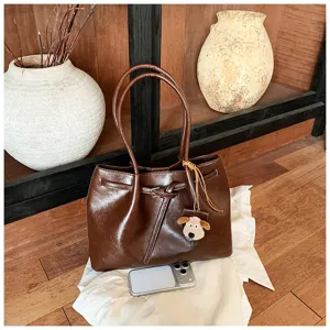 Brown PU leather tote bag close-up showing cute plush dog charm and chic belt accent.